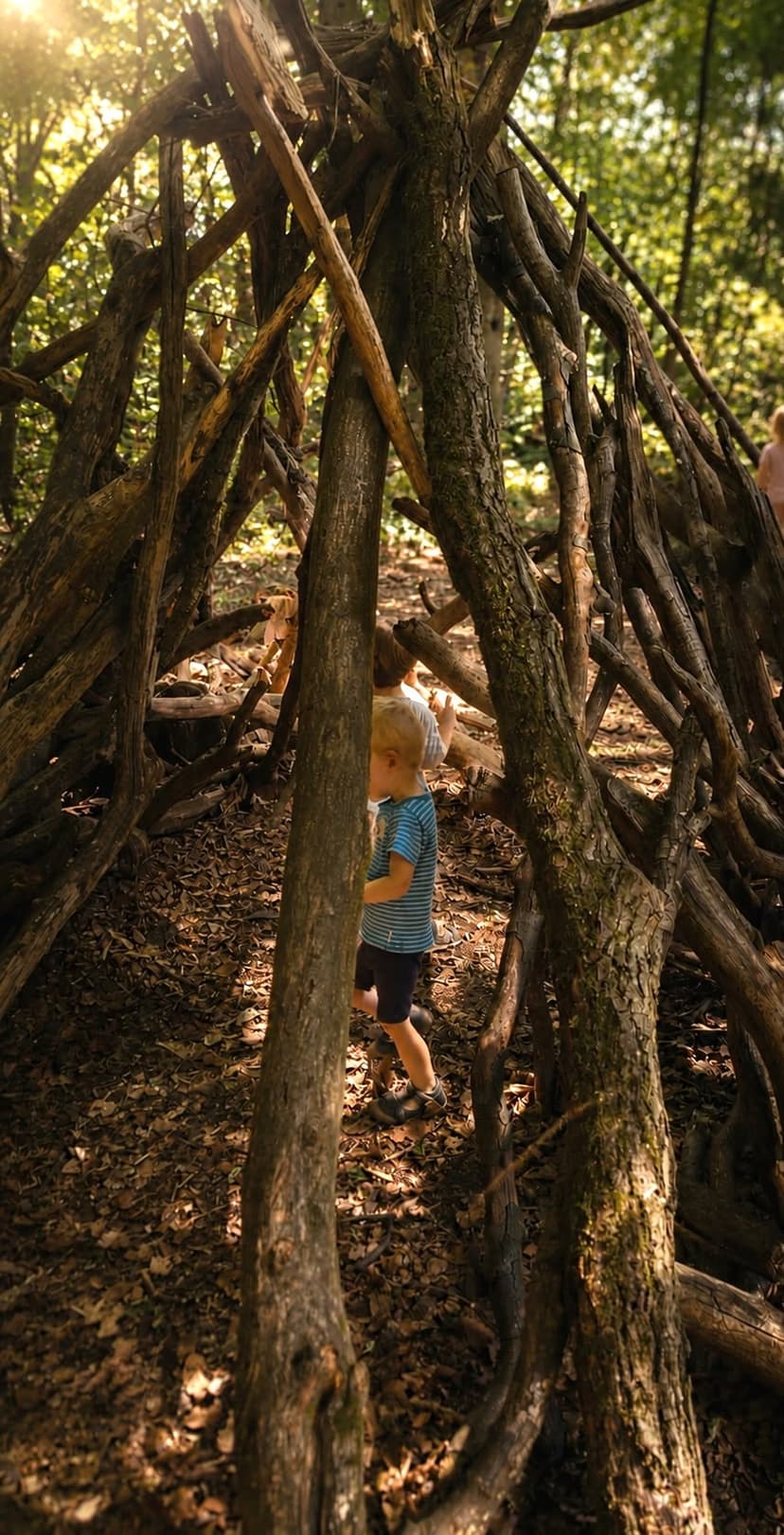 Kinder spielen in einem Tipi aus Ästen im Wald